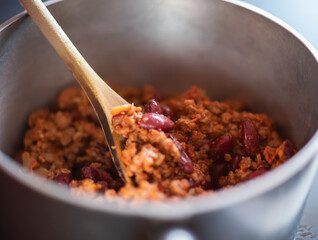 Close up and selective focus of a meat chilli concarne cooking on the hob in a stainless steel saucepan with shallow depth of field and bokeh