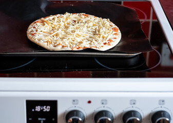 Close and selective focus of a readymade frozen stone baked thin four cheese pizza on a baking mat...