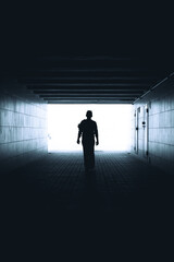 The woman walks down the tunnel towards the light. Silhouette of a woman walking in the underpass