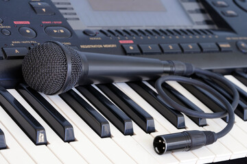 The black microphone lies on the keyboard of the synthesizer. Musical instruments. Karaoke and vocals. Art.                               