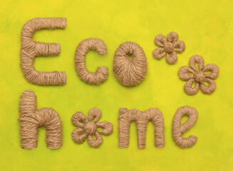The inscription lettering eco home made of eco-friendly material on a green-yellow background decorated with flowers from a string of rope love of nature and environmental friendliness