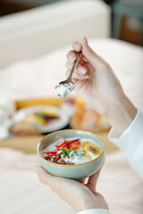 Hands of woman eating granola with fruit slices and non-dairy yogurt for breakfast