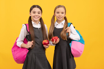 Hungry kids in formal uniforms hold vitamin apples for school snack yellow background, snacking