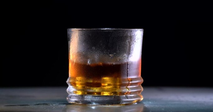 Super slow motion of droping the ice into the whiskey.