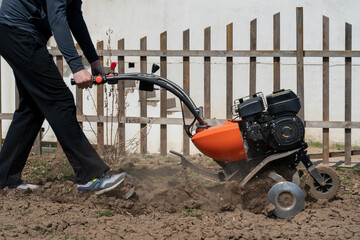 A young man digs the ground in the garden with a motorcultivator