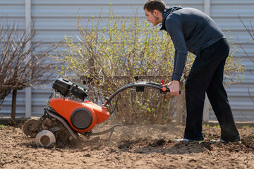 Fototapeta na wymiar A young man digs the ground in the garden with a motorcultivator