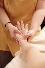 Close-up image of beautician massaging hands of female client to restore balance in the body and decrease anxiety