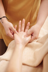 Close-up image of masseuse massaging palm of young woman to release tension and decrease anxiety