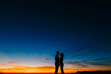 Silhouettes of a couple holding hands against the background of the sunset in the mountains