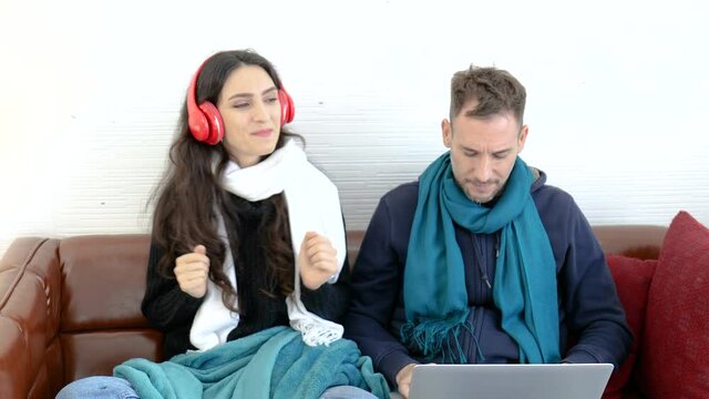 Woman listening to music while her boyfriend is working on his laptop.