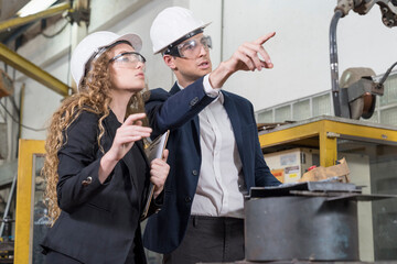 The engineer is explaining the operation of the machine to the manager. Man and woman talking and using tablet computer with robot arm production line.