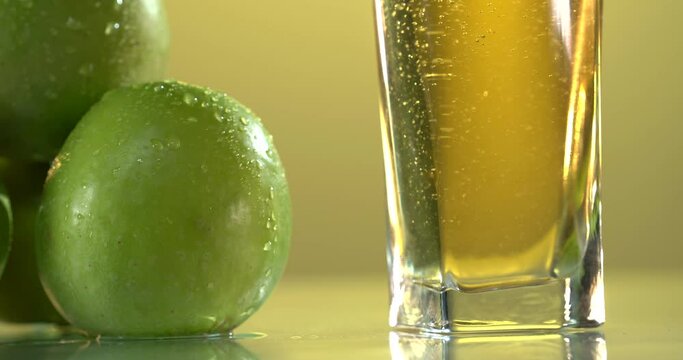 close-up of pouring juice into a glass. there are fresh green apples on the table nearby