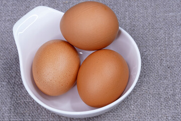 Three brown chicken eggs in a white round bowl top view. Eating raw foods. Proteins.                               