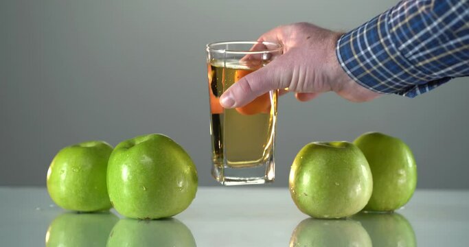 Man's hand takes the glass with apple juce from the table. There are fresh green apples near