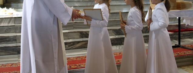 Three girls in white dresses and Catholic priest while celebrate First Holy Communion into church
