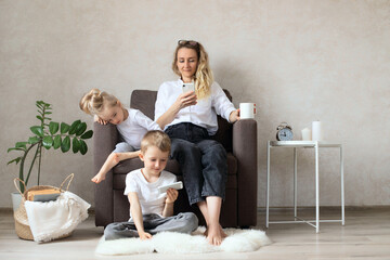 Fototapeta premium Mother and children are sitting in the living room on a chair with phones in their hands.