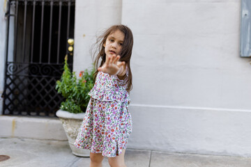 Beautiful little girl in flowered dress posing in front of a gray wall