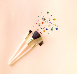 Set of three makeup brushes on a pink background, top view with copy space. Cosmetic products. Background is complemented by sparkles in the form of stars and round ones.
