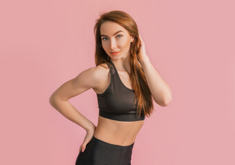 Fitness girl smiling in black sportswear on a pink background. Slim woman with a beautiful athletic body and tanned skin