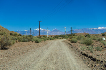 Fototapeta na wymiar Gravel road in an arid place leading to the andes mountains with electric poles.