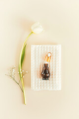 Minimalistic, spa natural, cosmetic composition with white towel, glow serum bottle and tulip on a light background. Wellness, home skin care and relax treatment concept. Top view