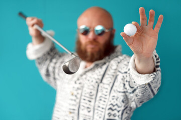 Naklejka premium A guy with a bald head and a lush beard holds in his hands a golf club and a ball. A man with glasses and a shirt. Golf player. Sports and Entertainment 
