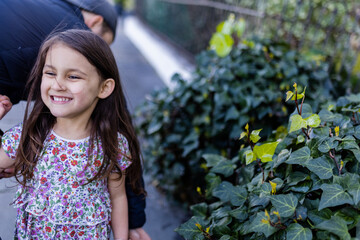 Happy and cute little girl in flowered dress standing next to a bush