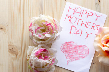 Close up flat lay view of a Happy mother's day greeting card and two flowers on a wooden table