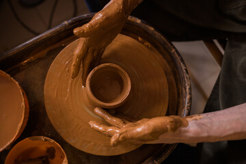 close-up of a man's dirty hands making a mug out of clay on a loom in a room