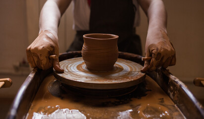 close-up of a man's hands cutting off a clay mug with a wire on a loom in a room