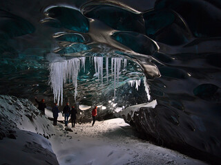 Group of tourists exploring the Sapphire Ice Cave, located in Breiðamerkurjökull glacier, Vatnajökull, Iceland, on a tour with a moulin hole in the blue shimmering ceiling and icicles hanging down.