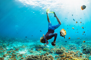 Happy family vacation. Man in snorkeling mask with camera dive underwater with tropical fishes in...