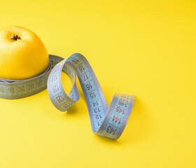 Yellow apple and a centimeter tape, on a yellow background. Healthy food concept. Side and top view. Copy space, selective focus.