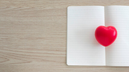 Top view of red heart love on an open and empty notebook on wooden background with copy space.