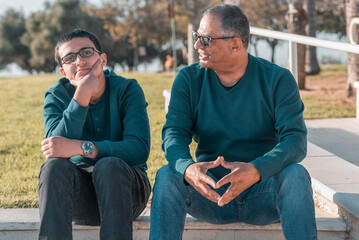 Teenager son and senior father sitting on stairs outdoors at home and talking.