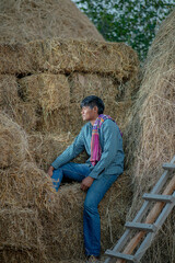 Naklejka na ściany i meble Farmer resting sitting by the haystack.relaxing on summer field with hay stacks. Fresh