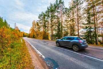 Turn the country broken road. The car goes on the road. Mixed forest. Sunset over the forest lake. Autumn weather. Beautiful nature. Russia, Europe. View from the side of the road.