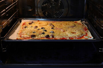 Homemade pizza in oven. Smelting or melting cheese. With ham, olives, tomato sause and pineapple. Stockholm, Sweden.