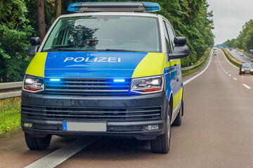 German police car on a lane and hard shoulder of a motorway. switched on headlights and flasher on...