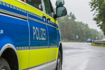 Passenger side of a German police car. View of the lettering Police on the body with the exterior mirror. Blue background and yellow color with reflective stripes. Asphalt road in rainy weather