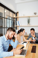 Serious man reading news on smartphone when his colleagues discussing fresh memes in background during coffee break