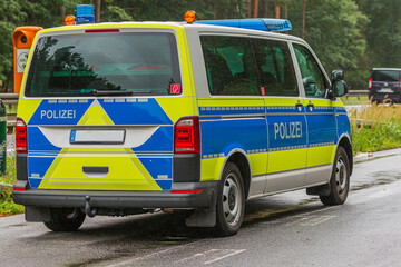 German police car in an emergency stop on the highway next to an emergency telephone. Rainy weather and wet road surface. View of the vehicle body on the passenger side and the police lettering