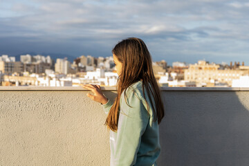 Fototapeta na wymiar Cute preteen girl looking worriedly at the city from her terrace at sunset