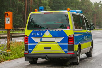 Police car in an emergency bay on a motorway in the state of Brandenburg. Emergency telephone on the roadside. two-lane highway with asphalt surface in rainy weather. Guard rail and trees