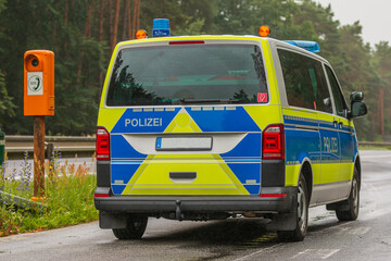 German police car on a motorway in the state of Brandenburg from a side view. Emergency telephone in an emergency bay on the side of the road. two-lane highway with asphalt surface in rainy weather