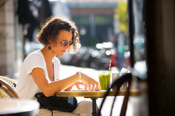 healthy woman having a green juice reading on a sunny terrace