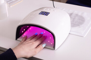 Female hand with manicure nails in gel polish lamp in beauty salon