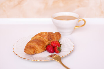 Coffee cup and sweet croissant with fresh strawberry on white table