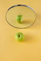 The Green Apple is reflected in the mirror where it sees itself as bitten, on a yellow background