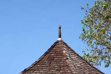 Old shingle rooftop with a carved tip under blue sky